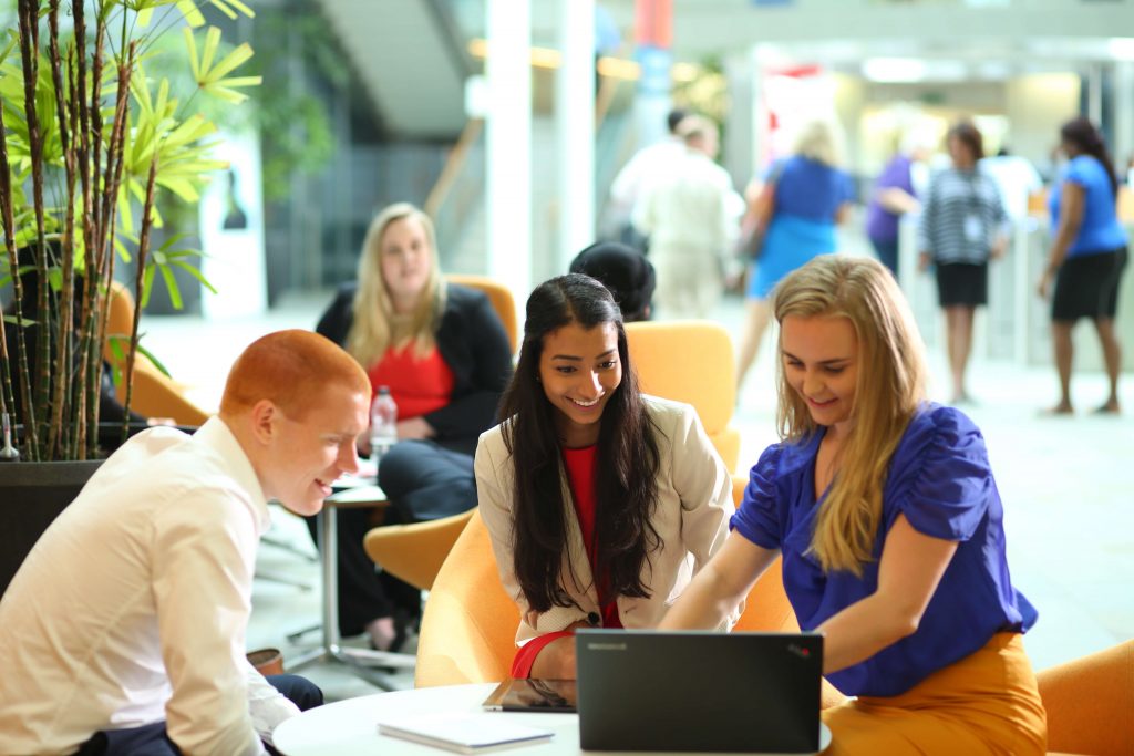 Graduates working in breakout area around laptop