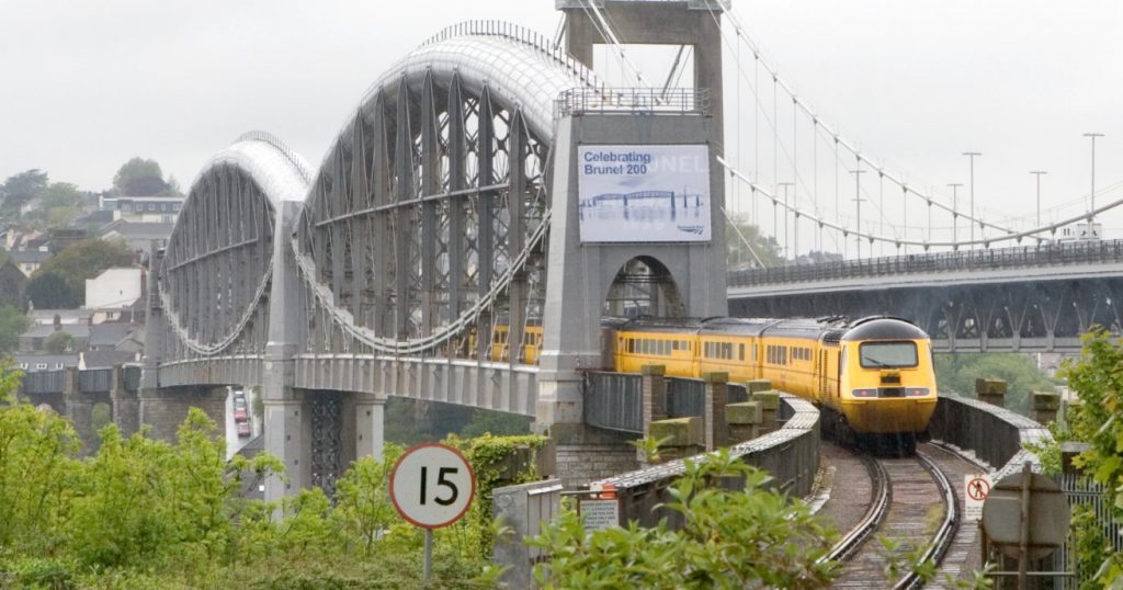 A yellow engineering train drives across the Royal Albert Bridge, daytime