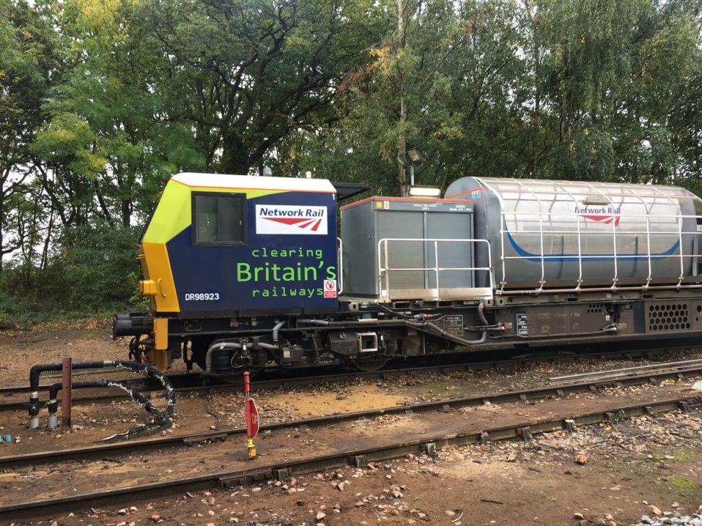 A Leaf busting train, on the tracks in the Autumn, with the messaging "clearing Britain's railways" written on the side