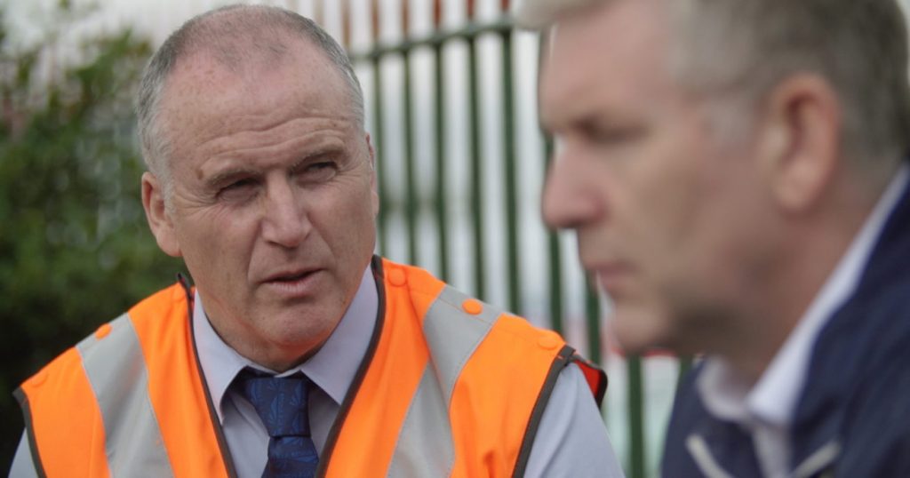 A Network Rail worker in an orange high visability jacket, speaking to someone who looks concerned on a railway platform. This is a still image from the Samaritans Small Talk Saves Lives film