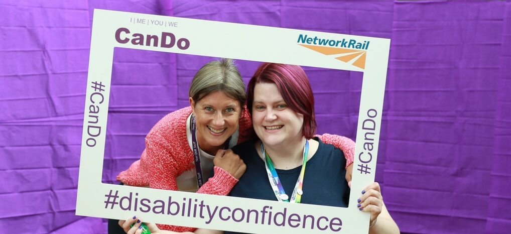 Members of CanDo posing in front of a purple background, holding a mock picture frame