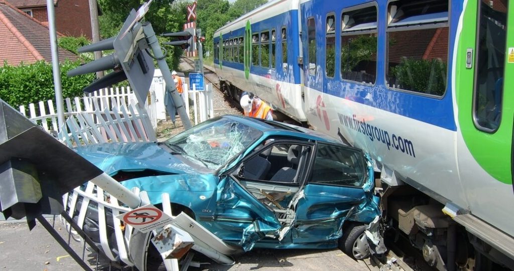 Smashed-up car by train near level crossing