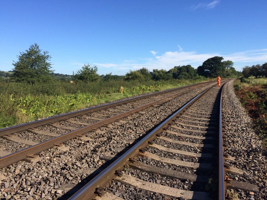 A railway worker stands on the tracks in the distance on a hot, sunny day.