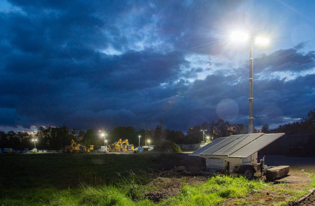 Solar panels at a railway project with diggers in the background, nighttime