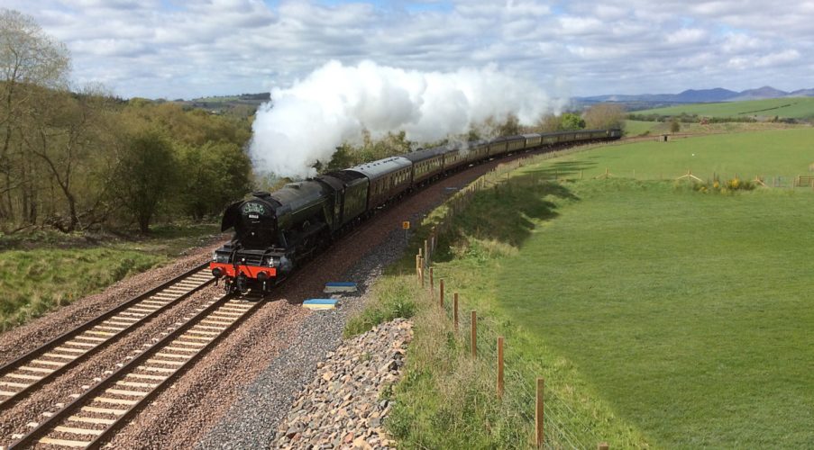 Steam train travelling along Borders Line surrounded by fields.