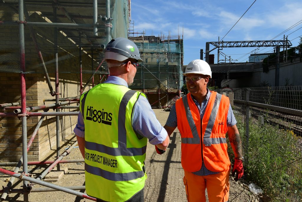 A Network Rail worker and a project manager on a work site wearing full PPE, shaking hands.