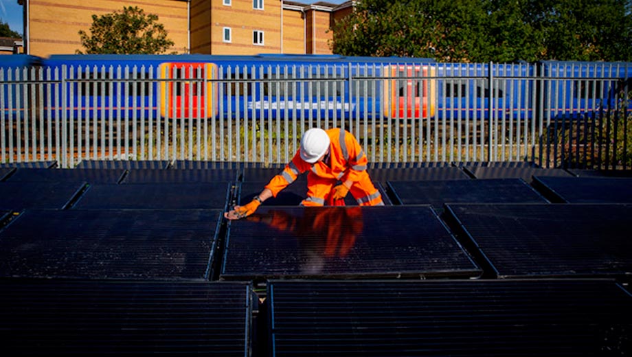 A rail worker cleans solar panels beside the railway, daytime