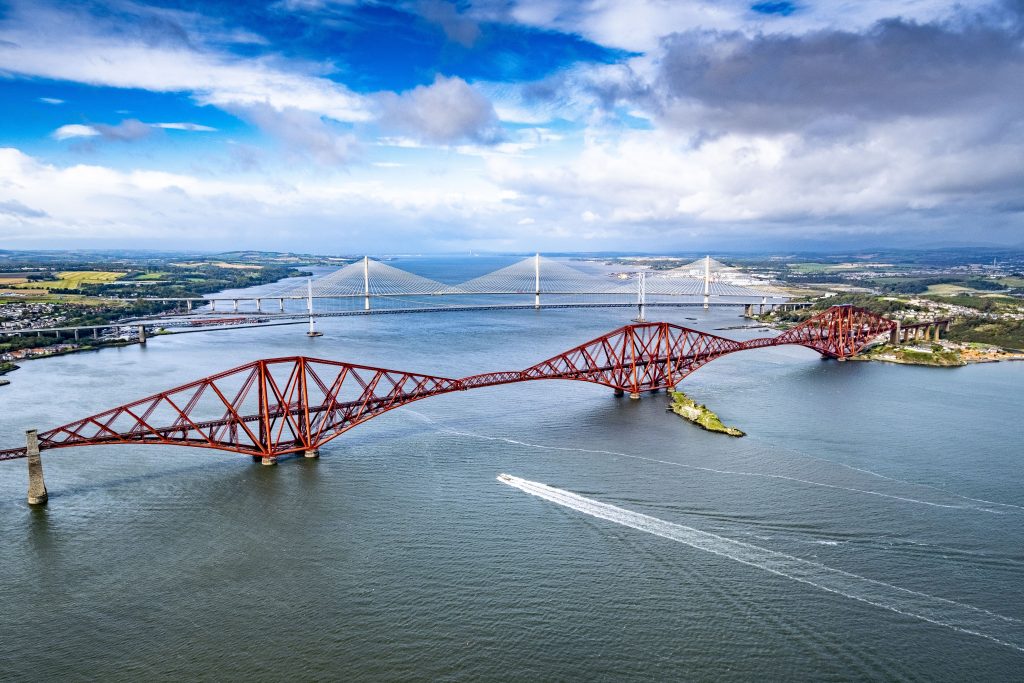 Aerial shot of Forth Bridge with blue skies, sea and boat travelling underneath