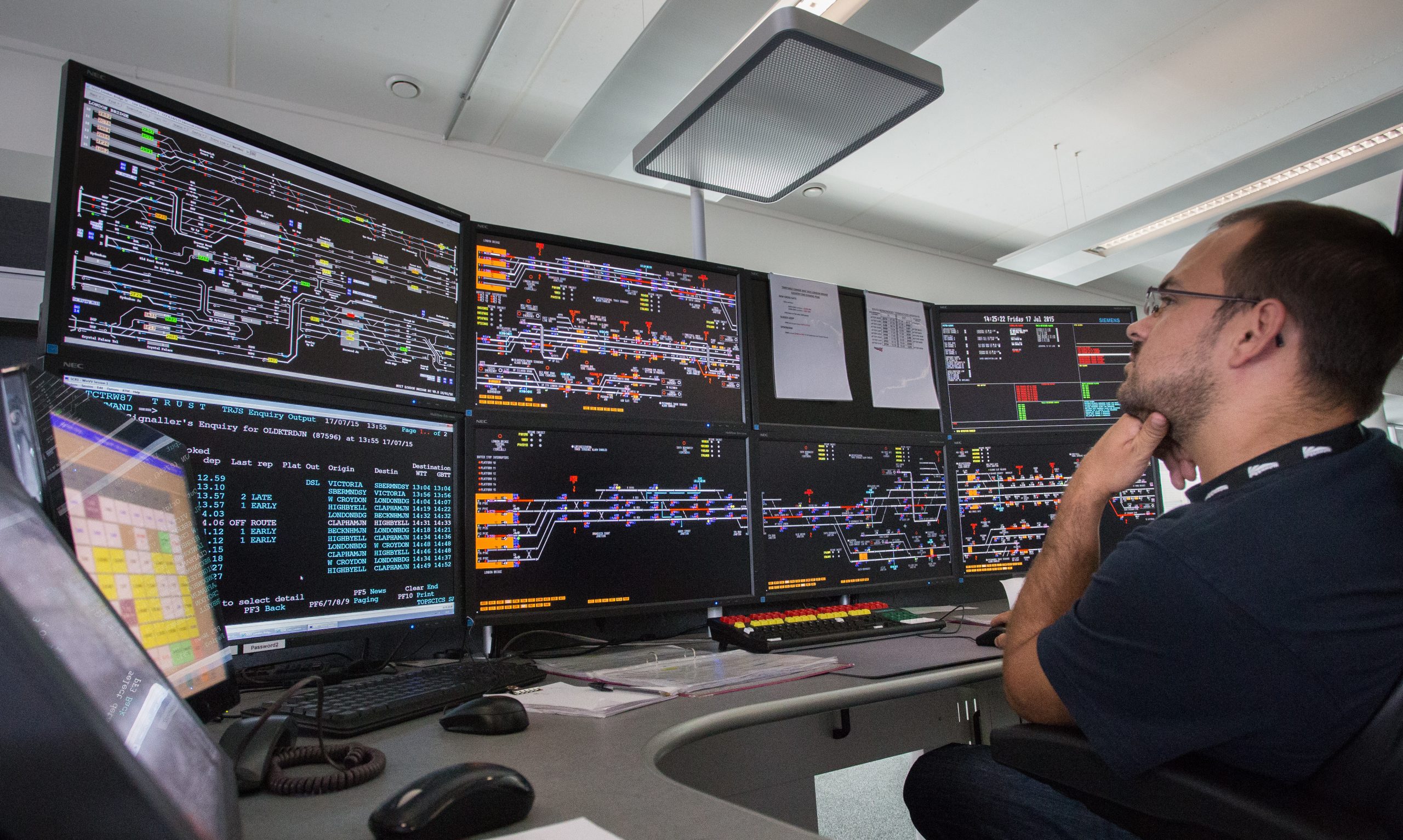 Network Rail signaller, looking at large computer screens showing the rail network.