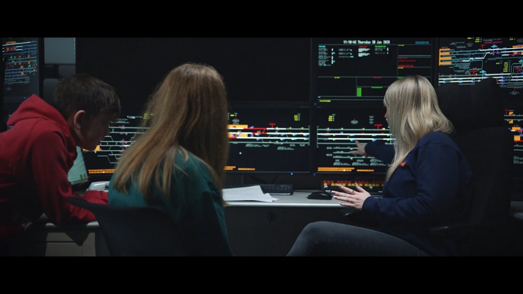 A young girl sits beside a female signaller at a digital screen showing the signalling system.