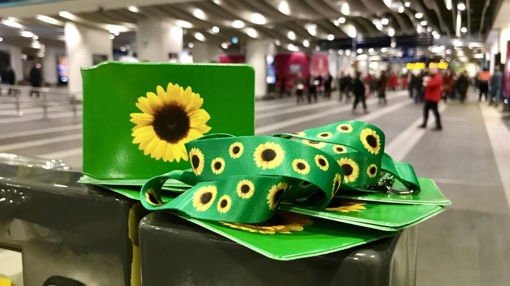 A sunflower lanyard and sunflower ticket holder on a desk at a busy station