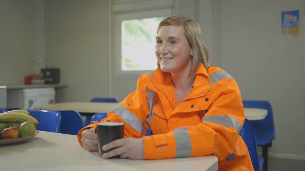 A female engineer sat in full PPE with a cup of tea