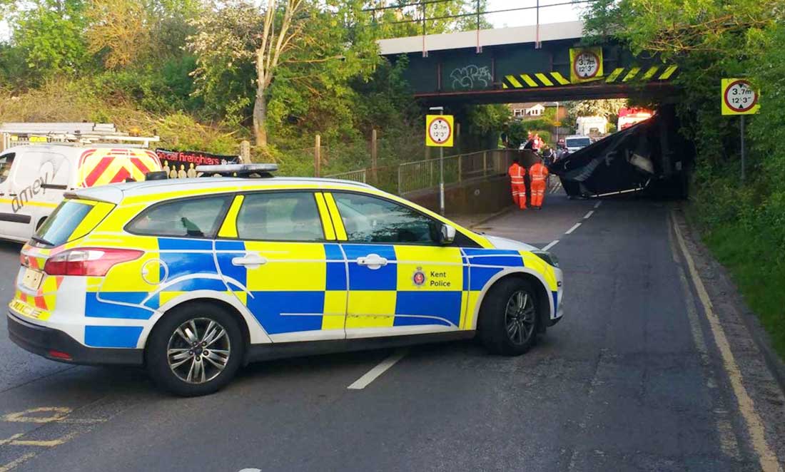 Police car blocking the road after a bridge strike, with Network Rail workers in the background