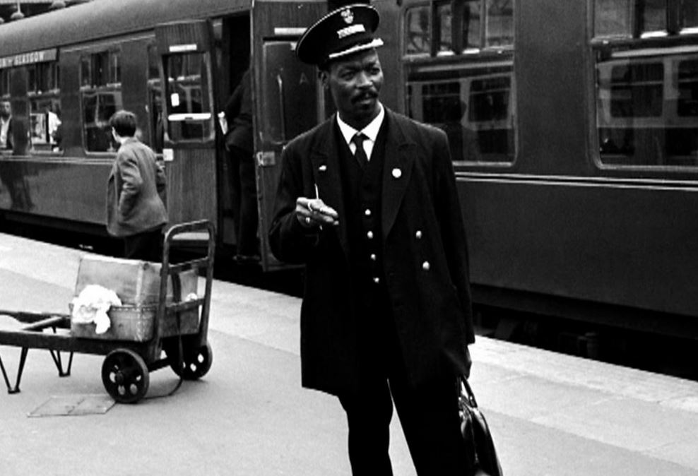 Asquith Xavier, the first Black train guard standing at Euston station in 1966