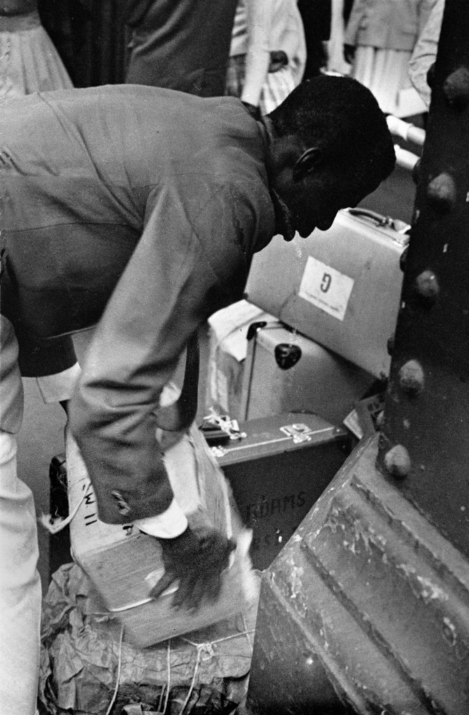 1960s photograph of the Windrush Generation arriving at London Waterloo - a man moving suitcases and boxes