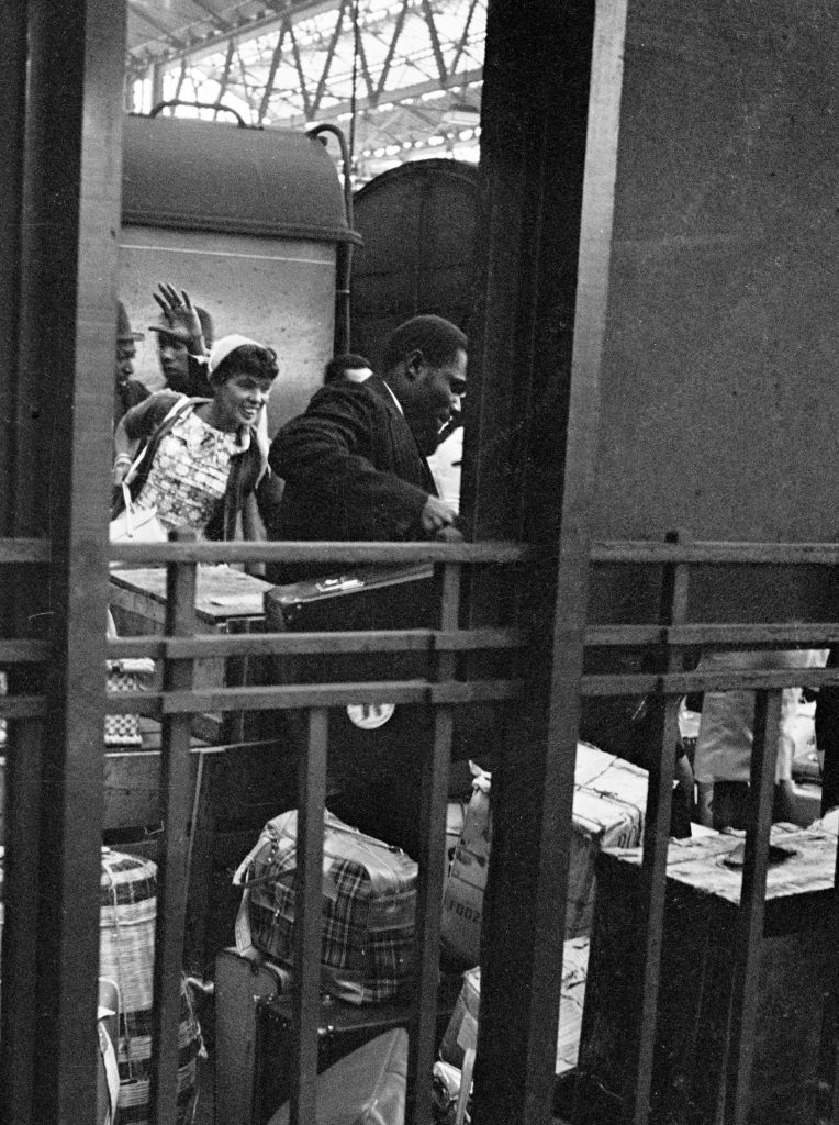 1960s photograph of the Windrush Generation arriving at London Waterloo - men and women moving luggage