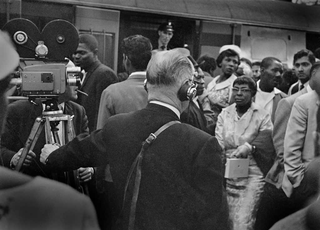 Black and white photograph of the last arrivals of the Windrush Generation at London Waterloo, captured by a contemporary film crew beside a train