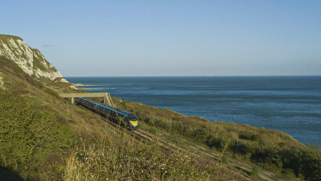 Train travelling through a cliff with the seaside next to it