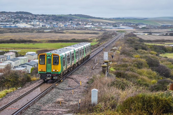 A green and yellow train travels through Newhaven as seen from Bishopstone station, daytime