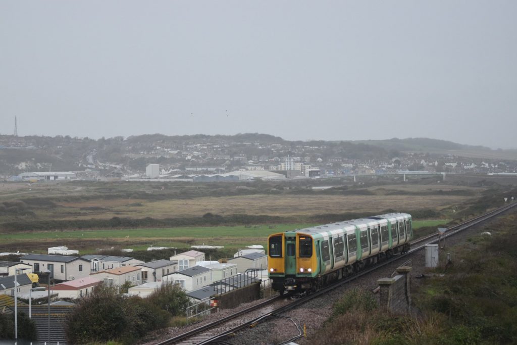 A green and yellow train in a foggy scene surrounding Newhaven, daytime