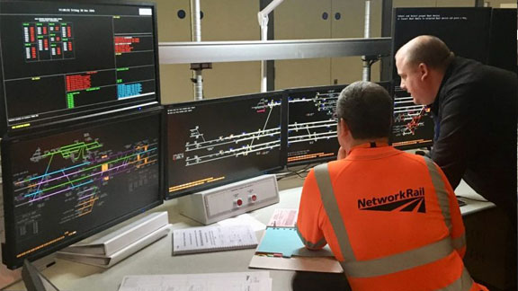 Two Network Rail workers, looking at computer displays in a Rail Operating Centre.