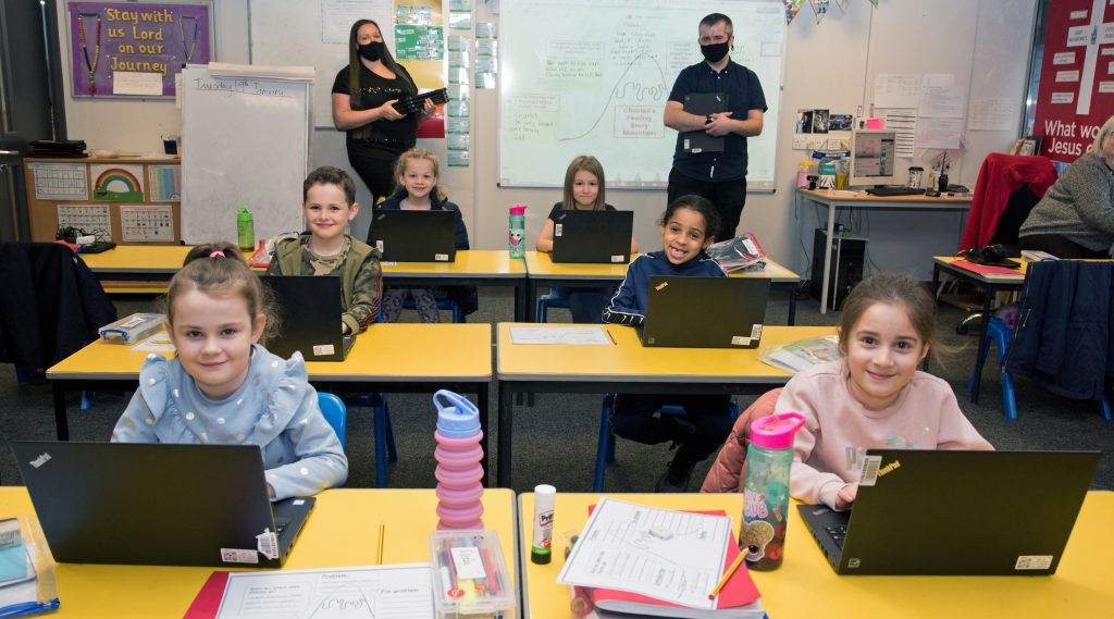 School children sitting at desks in a classroom with laptops donated by Network Rail. Teachers in background.