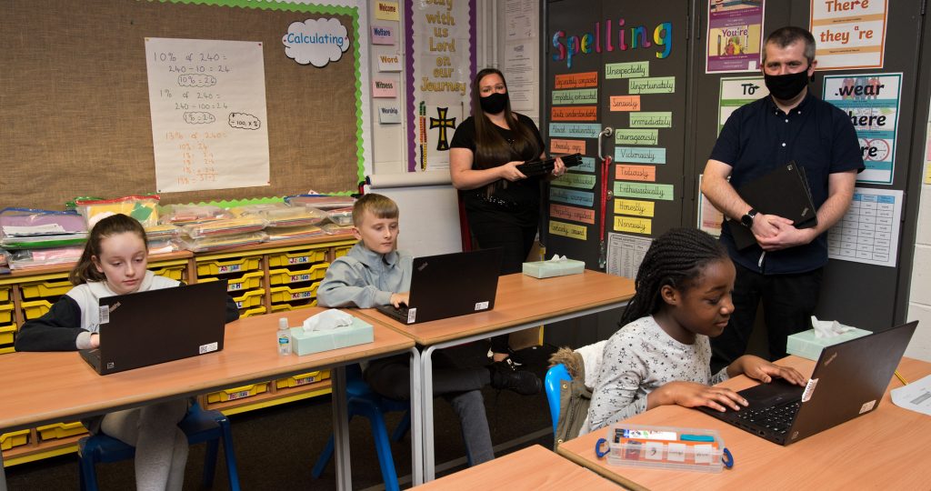 School children sitting at desks in a classroom with laptops donated by Network Rail. Teachers in background.