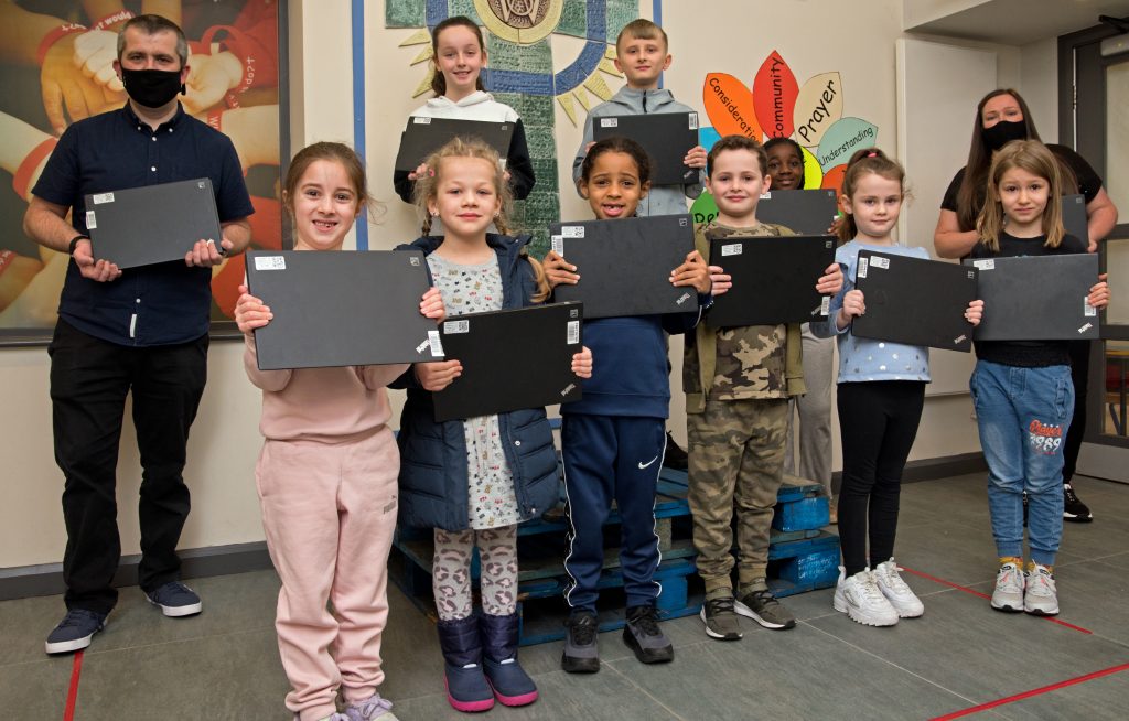 School children and teachers stand holding laptops donated by Network Rail.
