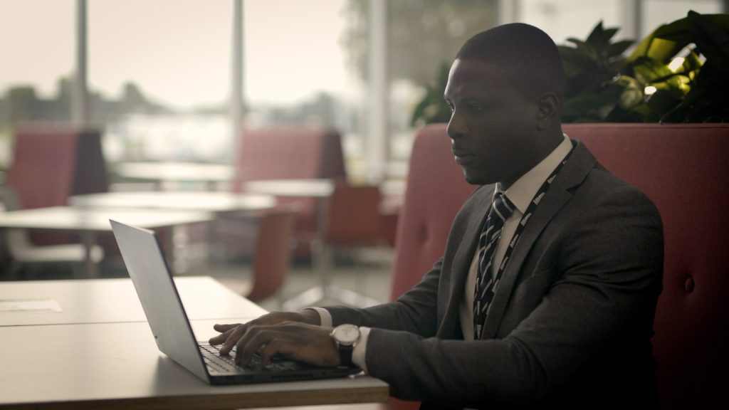 Graduate Adedayo Akeredolu sits at a laptop in an office canteen, daytime