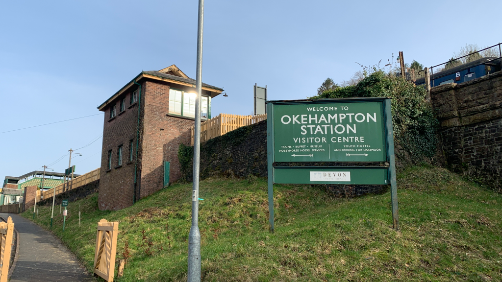 The approach to Okehampton station visitor centre with welcome sign in the foreground, daytime