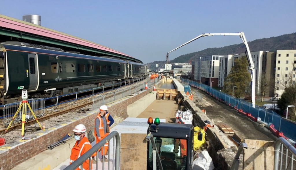 Frontline railway workers in PPE work next to a Great Western Railway train, daytime.