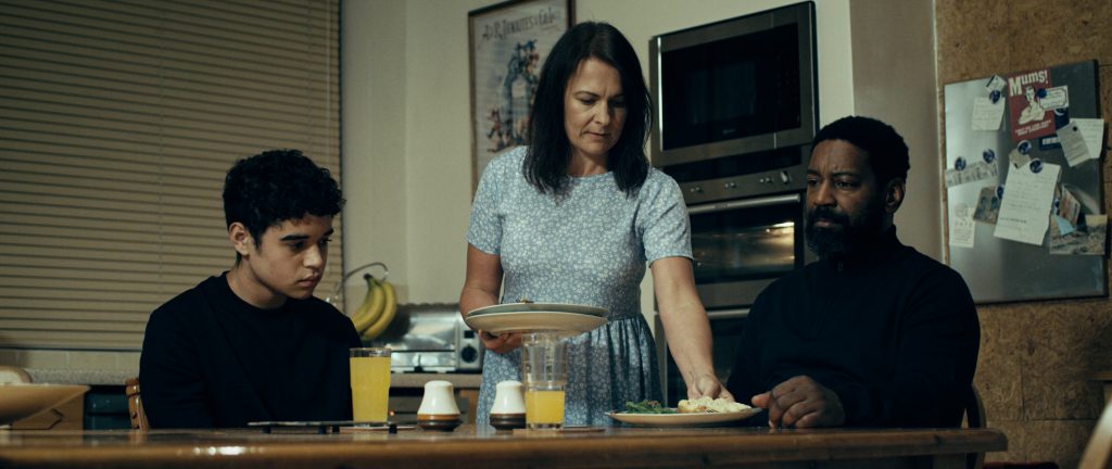 A father looks distant and upset during a family dinner with his partner and son.