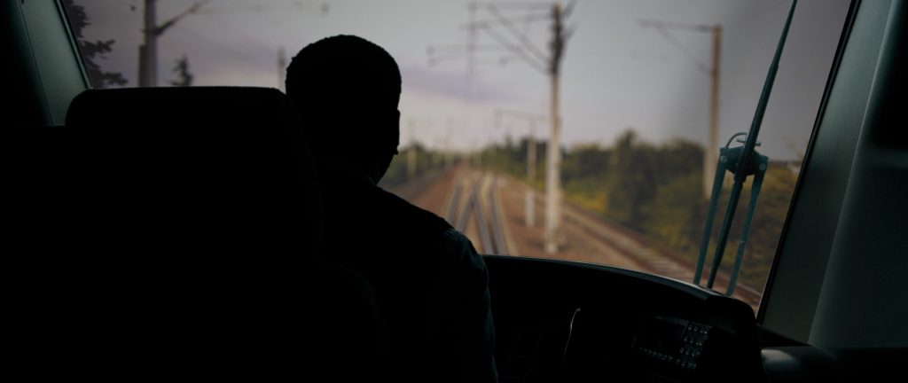 A silhouette of a train driver in the driver's cab looking down the tracks, daytime