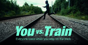 Male youth running across the tracks, daytime, with You vs Train campaign logo in foreground