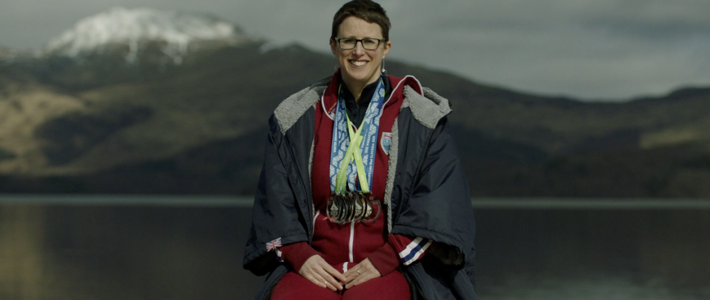 Ice swimmer and railway worker Jade Perry sits in front of a loch in Scotland wearing her ice swimming medals