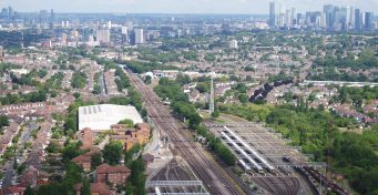 An aerial shot of tracks leading into London, with skyscrapers on the horizon.