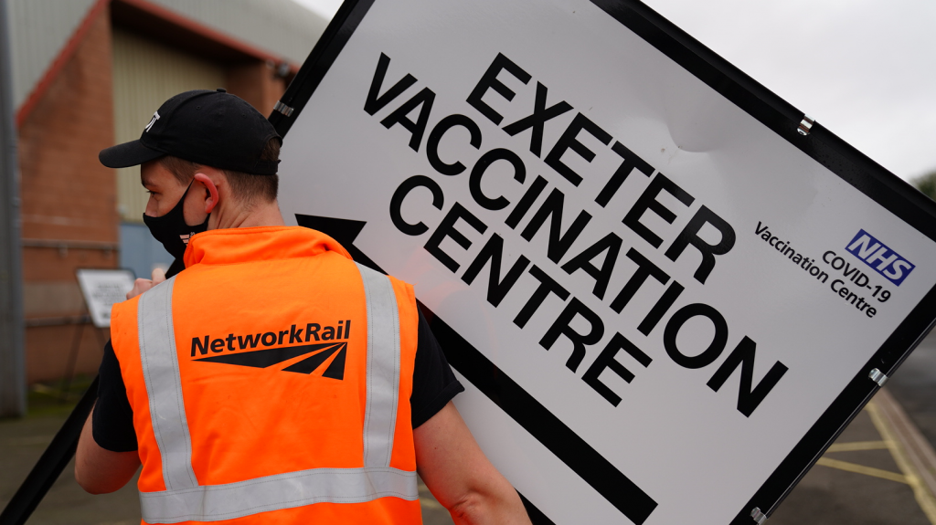 Network Rail volunteers help set up a mass vaccination centre in Exeter. Network Rail staff holding a sign to the centre.