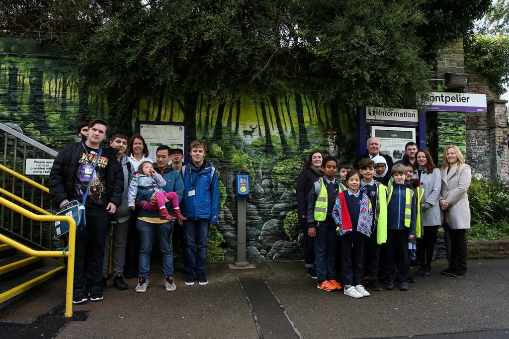 Adults and children in front of a Community Rail mural at Montpelier station