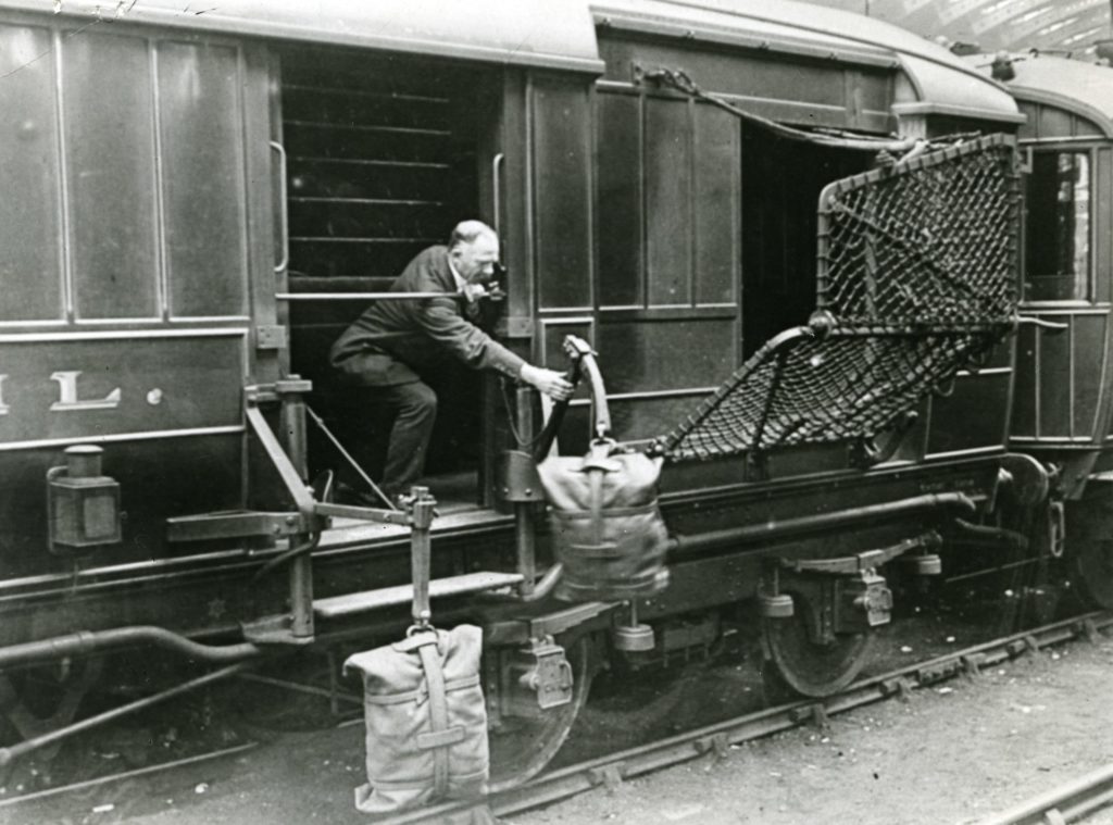 Black and white photo of a postal worker using trackside apparatus for mail bags, 1900