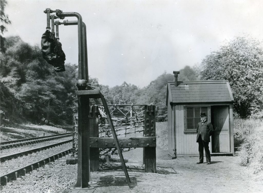 A man standing in a bowler hat beside trackside apparatus for Travelling Post Offices, 1908
