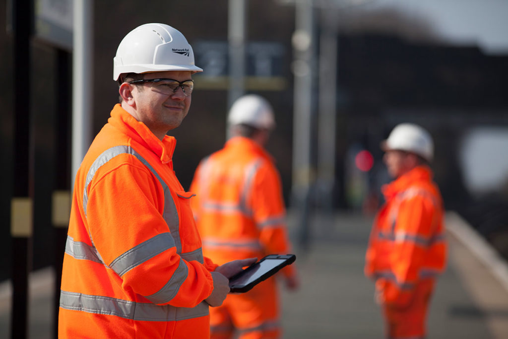 Engineer standing on a platform in full PPE uniform holding an iPad