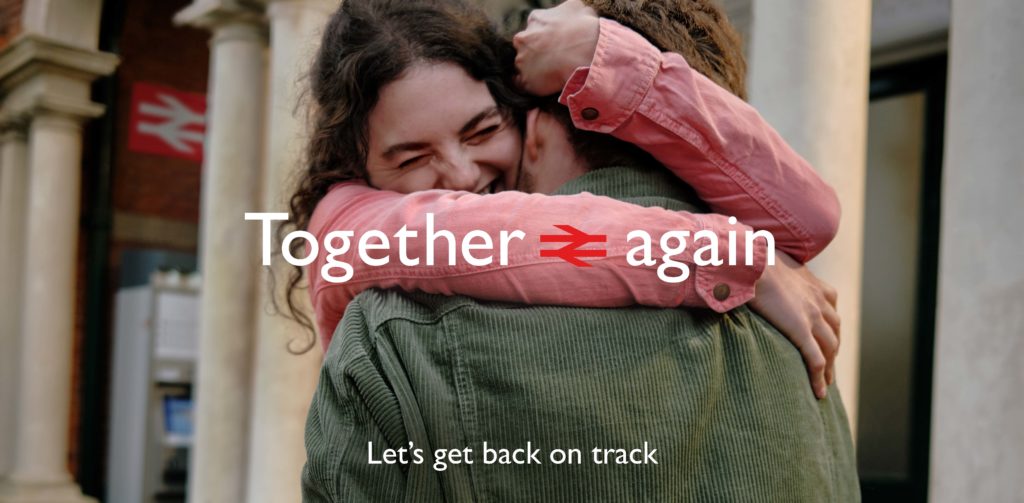 A man and woman embrace at a railway station with the text 'together again'