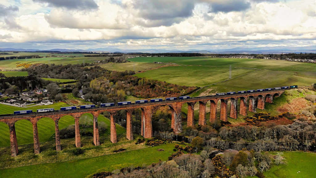 Freight train carrying Tesco containers over a scenic viaduct, daytime