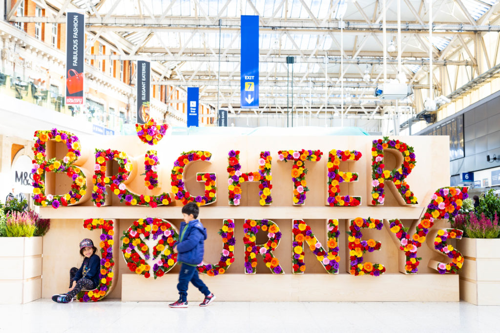 Children at a railway station in front of the words 'brighter journeys' written in flowers
