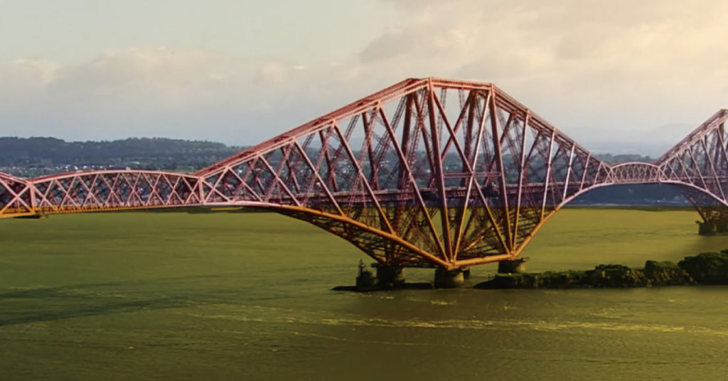 Imposing red iron rail bridge sits against a clear blue sky.