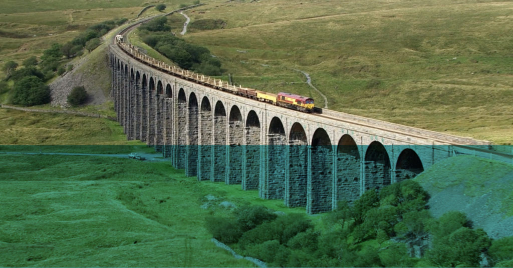 Freight train winds across a sweeping stone rail bridge through countryside to show the potential of civil engineering