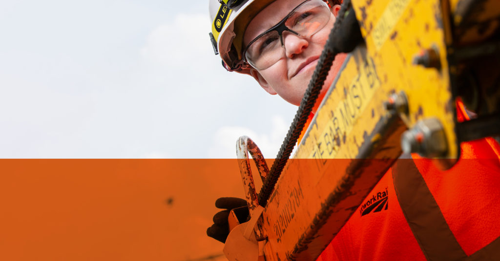 Rail graduate wearing hard hat and safety glasses leans over heavy duty equipment.