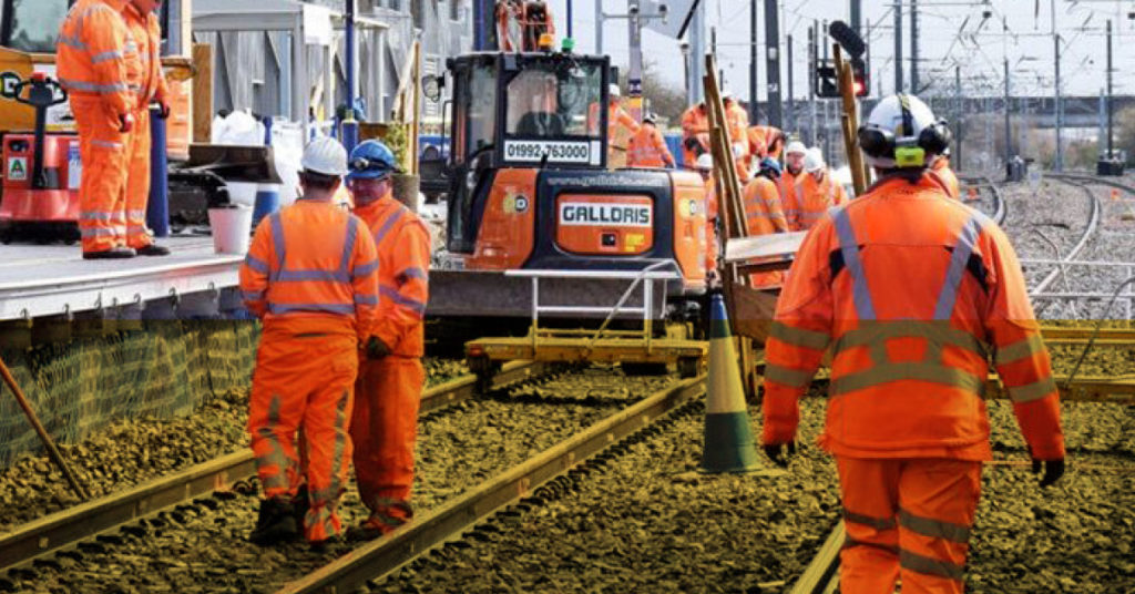 A group of Network Rail colleagues in full orange workwear perform electrical engineering tasks on the rails.