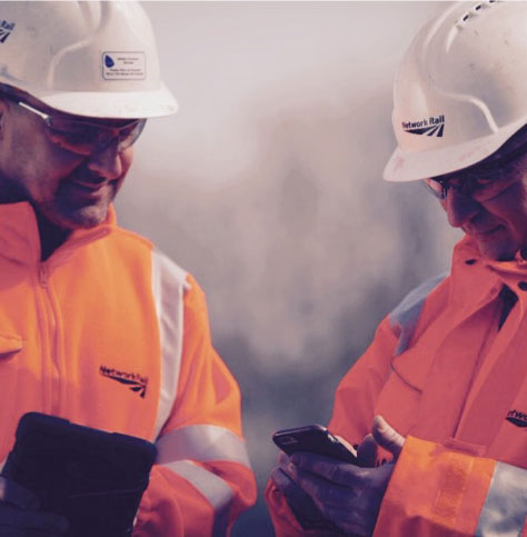 Two Network Rail engineers in full PPE looking at a mobile phone