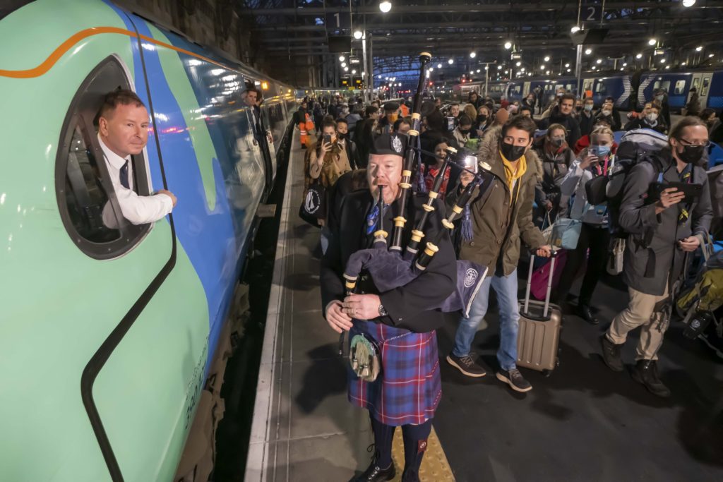A bag piper greets passengers on a platform at Glasgow Central for COP26